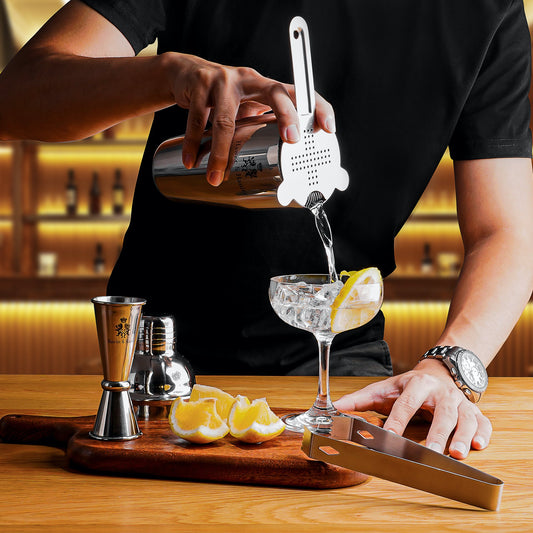 A man pouring a cocktail using a bartender kit shaker. There are lemons on a chopping board under the shaker.