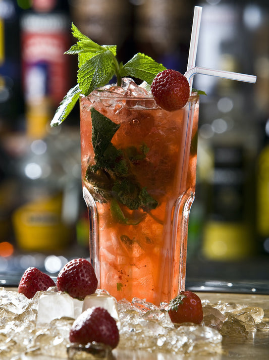 Red mojito in a cocktail glass with mint leaves, strawberries and a straw. It's sitting on a wooden table.